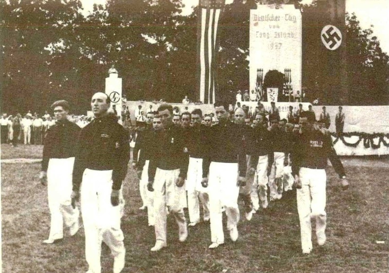 Two dozen young men marching with a American and German American Bund flag. 