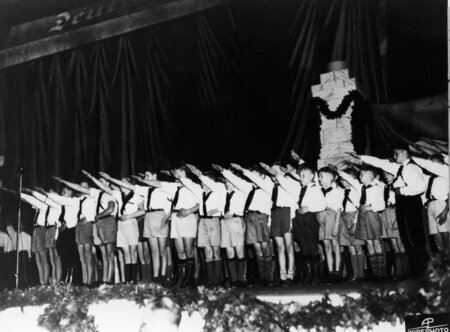 About two dozen young men and boys deliever the Nazi salute dressed in uniform. This moment was a part of the German Day celebration held at the camp.